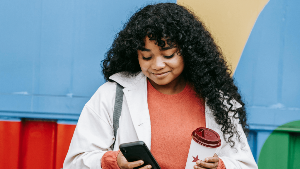 Junge Frau schaut auf ihr Smartphone: Mobiles Bezahlen - Vor- und Nachteile