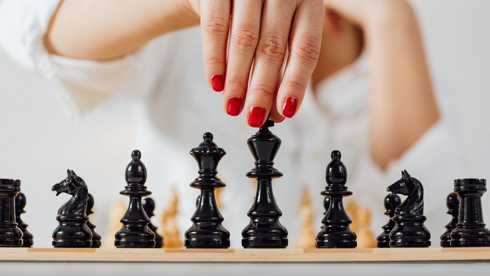 Schwarze Schachfiguren und weibliche Hand mit rotlackierten Fingernägeln